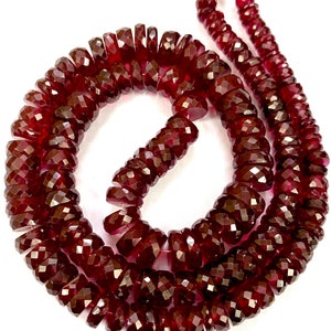 May include: A strand of deep red faceted gemstone beads. The beads are round and have a smooth, polished finish.
