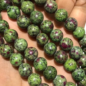 Puede incluir: Una hebra de cuentas de piedras preciosas verdes y rojas. Las cuentas son redondas y tienen un aspecto moteado.