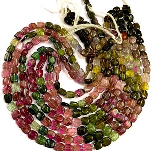 Puede incluir: Una hebra de cuentas de turmalina multicolores. Las cuentas son facetadas y tienen forma cuadrada. Las cuentas están enhebradas en un hilo blanco.