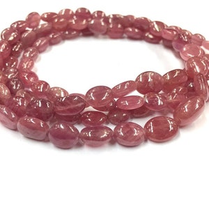 May include: A strand of pink oval-shaped gemstone beads. The beads are smooth and polished, with a slight shimmer.