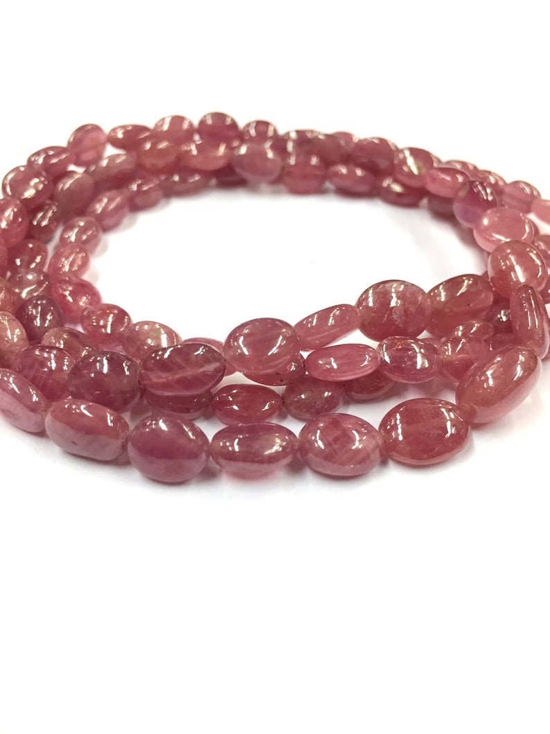 May include: A strand of pink oval-shaped gemstone beads. The beads are smooth and polished, with a slight shimmer.