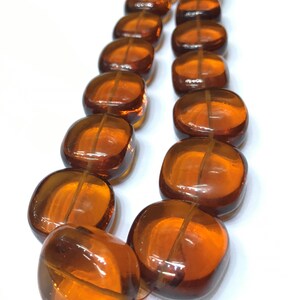 May include: A strand of amber-colored glass beads, each bead is square-shaped with rounded edges. The beads are strung together on a clear thread.