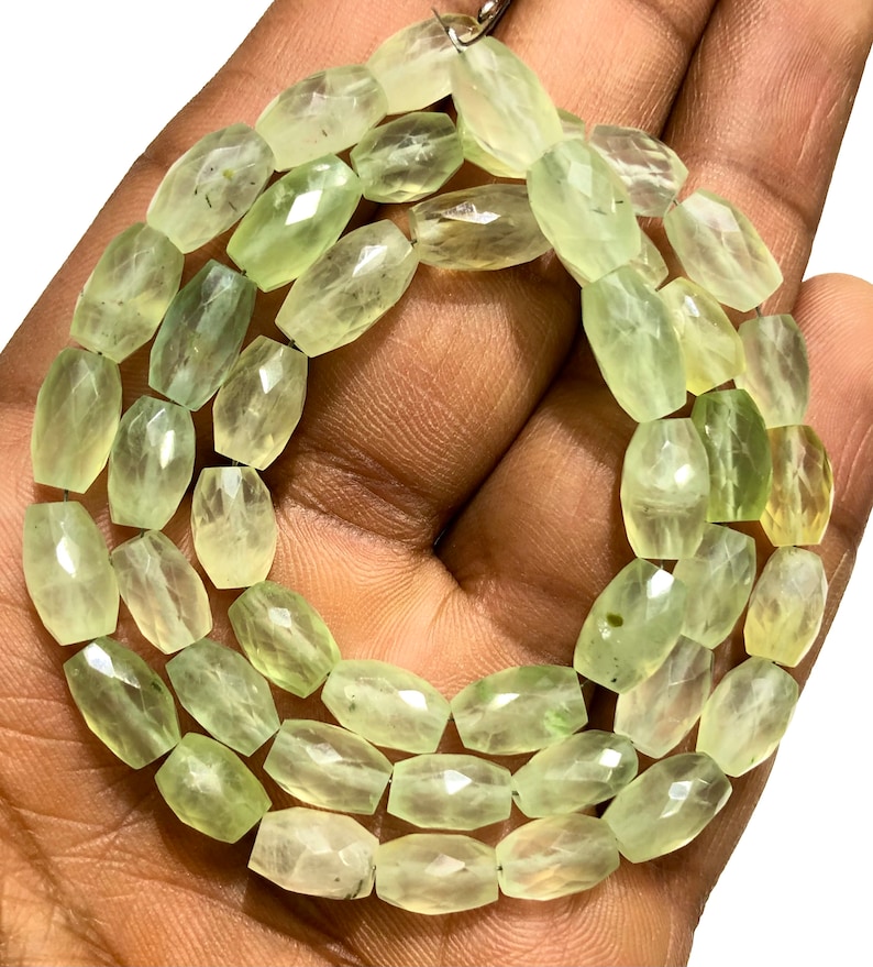 May include: A strand of light green faceted gemstone beads. The beads are oval shaped and have a smooth, polished finish.