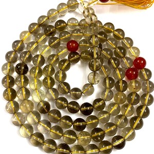 May include: A 108-bead mala necklace made of smoky quartz with gold accents. The beads are round and have a translucent appearance. The necklace is finished with a tassel.