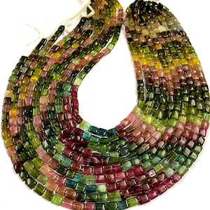 Puede incluir: Una hebra de cuentas de turmalina multicolores, cada cuenta tiene forma cuadrada con bordes redondeados. Las cuentas son una mezcla de verde, rosa y amarillo.
