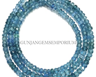 May include: A long strand of faceted, translucent blue gemstone beads arranged in a circular loop. The beads exhibit varying shades of deep and light blue with a reflective, polished surface. The text GUNJANGEMSEMPORIUM is printed in the center.