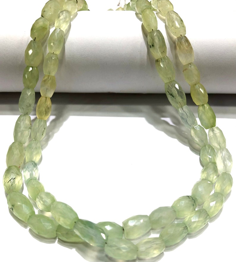 May include: A strand of light green gemstone beads, each bead is faceted and oval shaped.