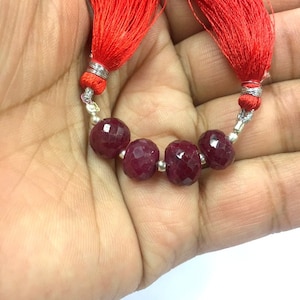 Może przedstawiać: Szereg sześciu fasetowanych koralików rubinowych z srebrnymi rozdzielaczami i czerwonymi frędzlami na obu końcach.