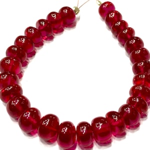 May include: A strand of deep red glass beads, each bead is round and slightly flattened, creating a unique shape. The beads are strung on a thin wire.