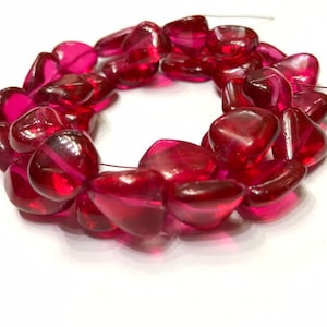 May include: A strand of pink heart-shaped glass beads. The beads are translucent and have a slight shimmer.