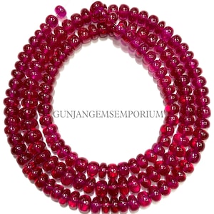 Può includere: Una collana o un braccialetto di perle di rubino rosso scuro, ogni perla è rotonda e liscia. Le perle sono disposte in un motivo circolare.