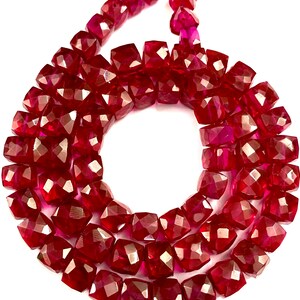 May include: A strand of deep red ruby gemstone beads, each bead is faceted and has a square shape.