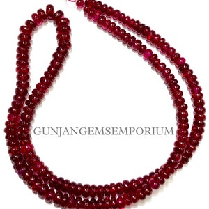 Könnte beinhalten: Eine Kette aus tief roten Rubinperlen, etwa 45 cm lang, mit einer glatten, polierten Oberfläche. Die Perlen sind auf einem dünnen Faden aufgefädelt und in einer doppelten Reihe angeordnet. Die Perlen sind alle gleich groß und gleichmäßig geformt und haben eine satte, leuchtende Farbe. Das Bild enthält den Text "GUNJANGEMSEMPORIUM".