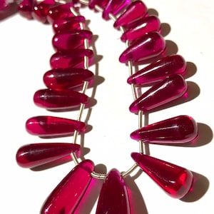 May include: A strand of deep pink faceted teardrop beads strung on silver wire. The beads are all approximately the same size and shape.