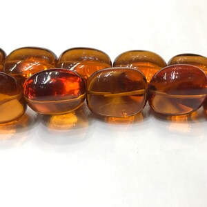 May include: A strand of oval-shaped amber beads. The beads are a rich, translucent brown color and have a smooth, polished finish.