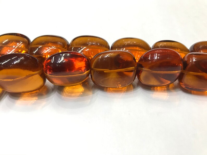 May include: A strand of oval-shaped amber beads. The beads are a rich, translucent brown color and have a smooth, polished finish.