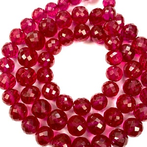 May include: A strand of deep red faceted gemstone beads. The beads are round and have a polished, shiny finish.