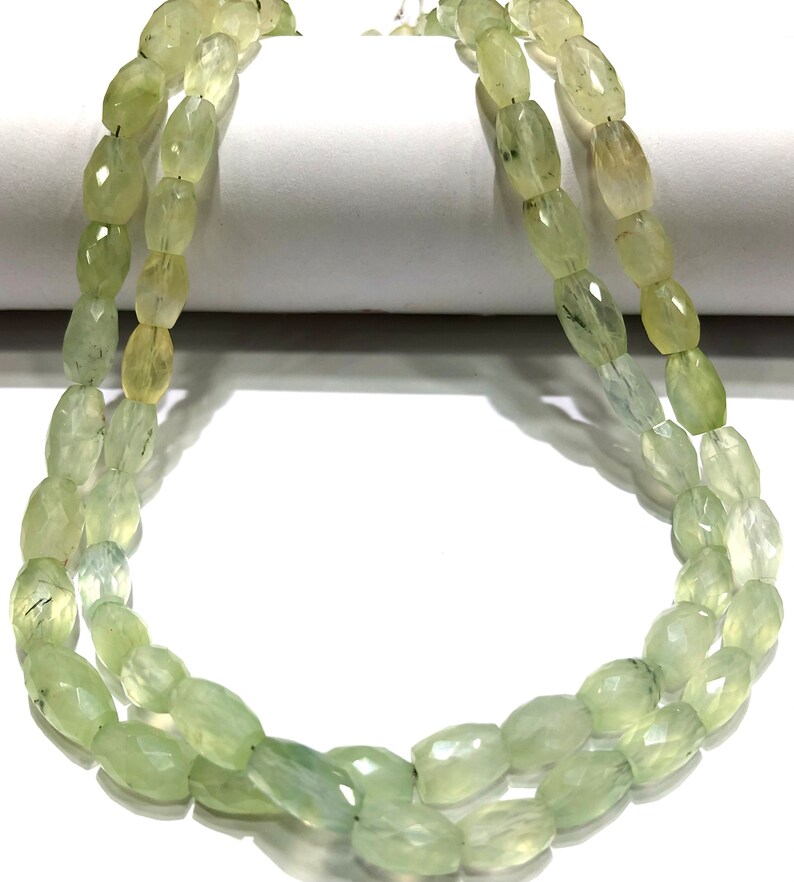 May include: A strand of light green gemstone beads, each bead is faceted and oval shaped.