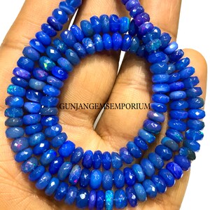 May include: A strand of blue opal beads, faceted and with a slightly iridescent finish. The beads are strung on a clear thread and are approximately 6mm in diameter. GUNJANGEMSEMPORIUM is printed on the image.