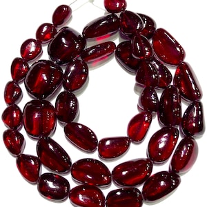 Puede incluir: Una hebra de cuentas de piedras preciosas de color rojo intenso, cada cuenta es lisa y de forma ovalada. Las cuentas están enhebradas en un cordón transparente y están listas para ser utilizadas en la elaboración de joyas.