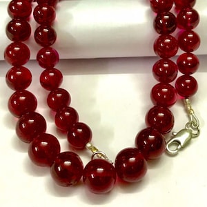 May include: A double strand necklace made of deep red glass beads. The necklace has a silver clasp.