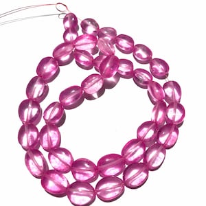 May include: A strand of pink oval-shaped glass beads. The beads are translucent and have a slight shimmer.