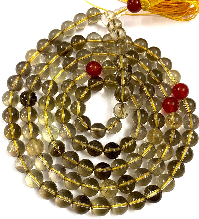 May include: A mala or prayer beads made of clear quartz with gold accents. The beads are strung on a cord and have a tassel at the end. There are three red carnelian beads interspersed throughout the mala.