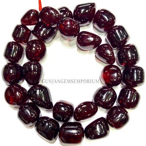 Puede incluir: Un collar de cuentas de piedras preciosas pulidas, de color rojo oscuro. Las cuentas son lisas, redondeadas y tienen un acabado brillante. La imagen incluye el texto "GUNJANGEMSEMPORIUM".