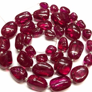 May include: A strand of deep red gemstone beads, each bead is a unique, irregular shape. The beads are strung on a silver wire.