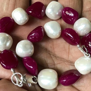 May include: A beaded bracelet featuring alternating white and deep red gemstones. The gemstones are irregularly shaped and strung together with a silver clasp. The bracelet is a jewelry item.