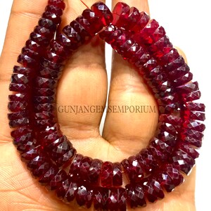 May include: A strand of deep red faceted gemstone beads. The beads are round and have a faceted finish. The beads are strung on a thin thread and are approximately 10mm in diameter. The beads are arranged in a circular pattern, with the ends of the strand overlapping. The beads are a rich, deep red color and have a high shine. The beads are perfect for making jewelry or other crafts.