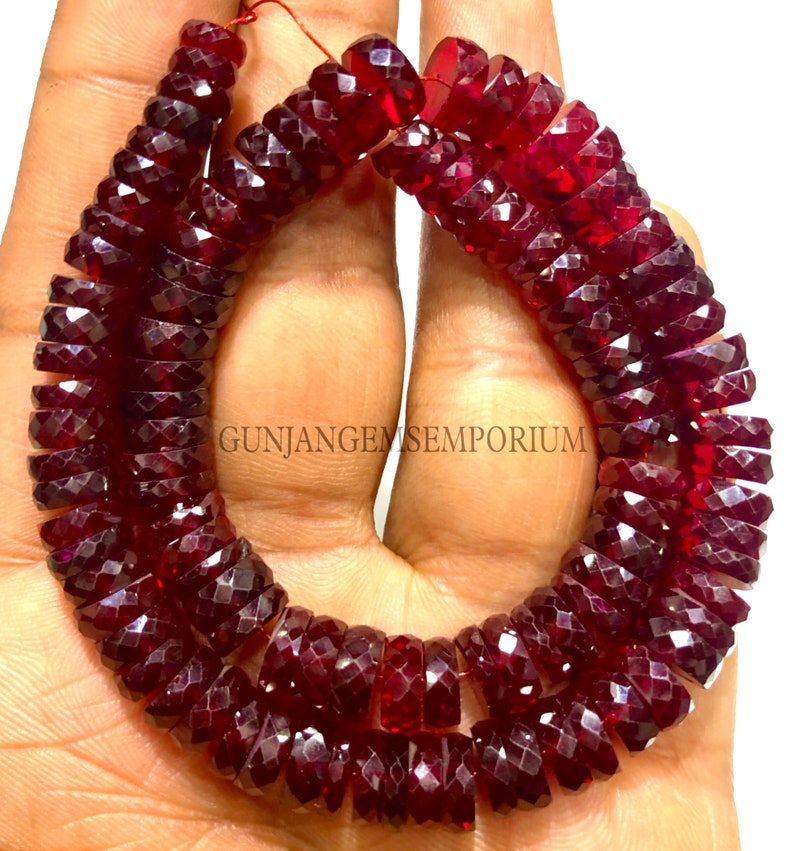May include: A strand of deep red faceted gemstone beads. The beads are round and have a faceted finish. The beads are strung on a thin thread and are approximately 10mm in diameter. The beads are arranged in a circular pattern, with the ends of the strand overlapping. The beads are a rich, deep red color and have a high shine. The beads are perfect for making jewelry or other crafts.