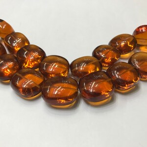 May include: A strand of amber-colored glass beads, each bead is oval-shaped and has a smooth, polished finish.