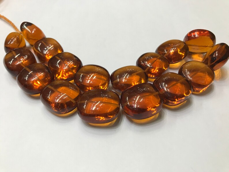 May include: A strand of amber-colored glass beads, each bead is oval-shaped and has a smooth, polished finish.