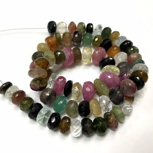 Op de afbeelding: Een streng facetgeslepen edelsteen kralen in verschillende kleuren, waaronder groen, roze, zwart en helder. De kralen zijn geregen op een zilveren draad en zijn ongeveer 6 mm in diameter.