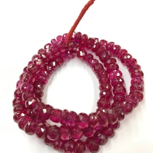 May include: A strand of deep red faceted gemstone beads. The beads are strung on a thin red cord.