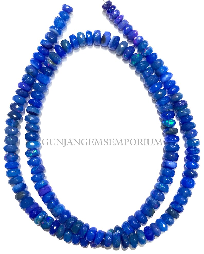 May include: A strand of blue opal beads, faceted and with a slightly iridescent finish. The beads are strung on a clear thread and are approximately 6mm in diameter. GUNJANGEMSEMPORIUM is printed on the white background.