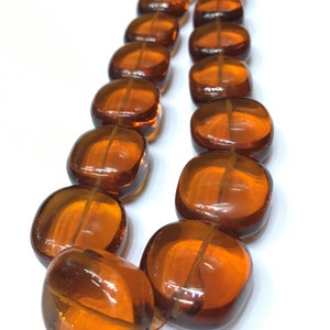 May include: A strand of amber-colored glass beads, each bead is square-shaped with rounded edges. The beads are strung together to form a necklace.