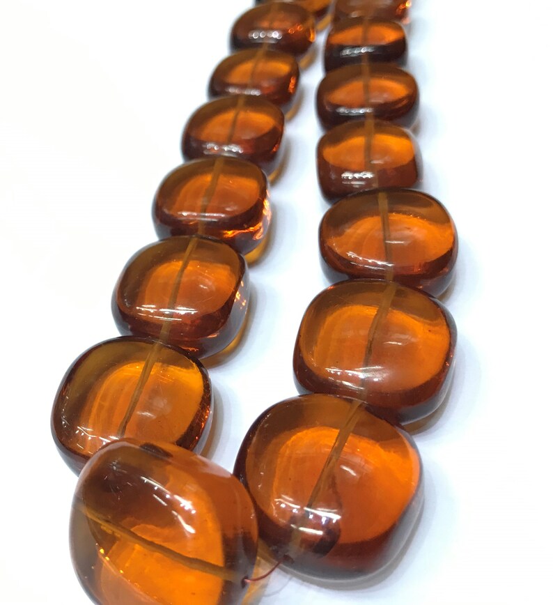 May include: A strand of amber-colored glass beads, each bead is square-shaped with rounded edges. The beads are strung together to form a necklace.