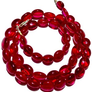 May include: A red glass bead necklace with oval-shaped beads. The necklace is coiled and has a silver clasp.