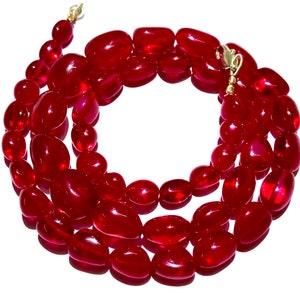 May include: A red gemstone necklace with oval-shaped beads. The necklace is made of polished, smooth stones and has a gold clasp.