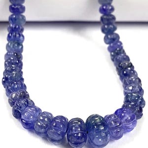 May include: A strand of blue gemstone beads, each bead is carved with a textured pattern. The beads are strung on a clear thread.