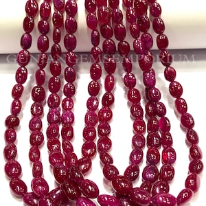 Puede incluir: Una hebra de cuentas de rubí rojo oscuro, cada cuenta tiene forma ovalada y está pulida para obtener un acabado liso y brillante. Las cuentas están enhebradas en un hilo transparente, creando un collar hermoso y elegante.