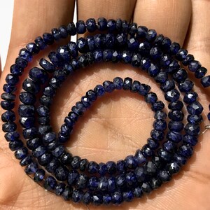 Può includere: Un filo di perle di zaffiro blu scuro, sfaccettate e con una forma leggermente irregolare. Le perle sono infilate su un filo sottile e hanno un diametro di circa 4 mm.