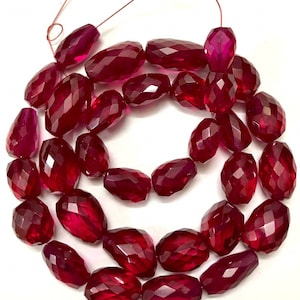 May include: A strand of deep red faceted gemstone beads. The beads are oval shaped and have a glossy finish.