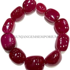 May include: A bracelet made of 10 smooth, deep red gemstone beads. The beads are oval-shaped and have a glossy finish. The bracelet is strung on a silver chain.