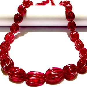 May include: A necklace made of deep red, oval-shaped beads. The beads have a textured, ribbed surface.