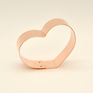 May include: A copper heart-shaped cookie cutter. The cutter is made from a single piece of metal and has a smooth, polished finish.