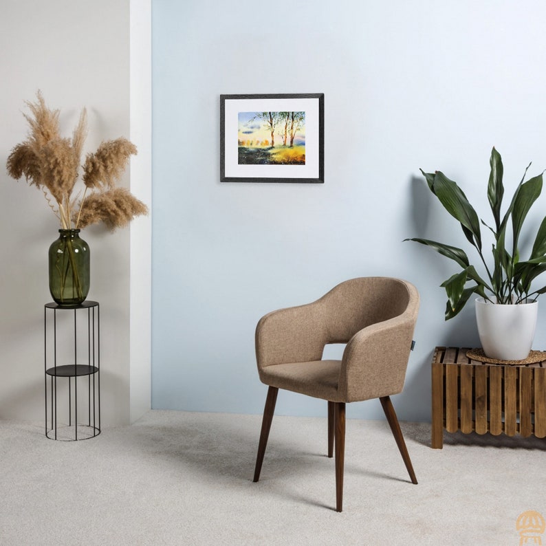 May include: A brown armchair with wooden legs sits in a room with a framed watercolor painting of a landscape and a potted plant on a side table.