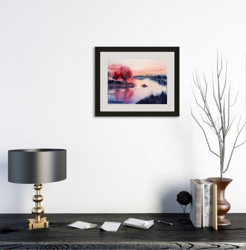 May include: Watercolor painting of a serene landscape featuring a river scene with vibrant red trees and a soft, colorful sky. The artwork is framed in a black frame, adding a touch of elegance to the tranquil scene. The painting captures the beauty of nature.